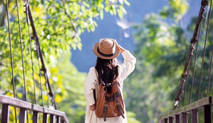 A woman in a hat and white dress walks a bridge, embodying travel beauty with Atria Tourist.